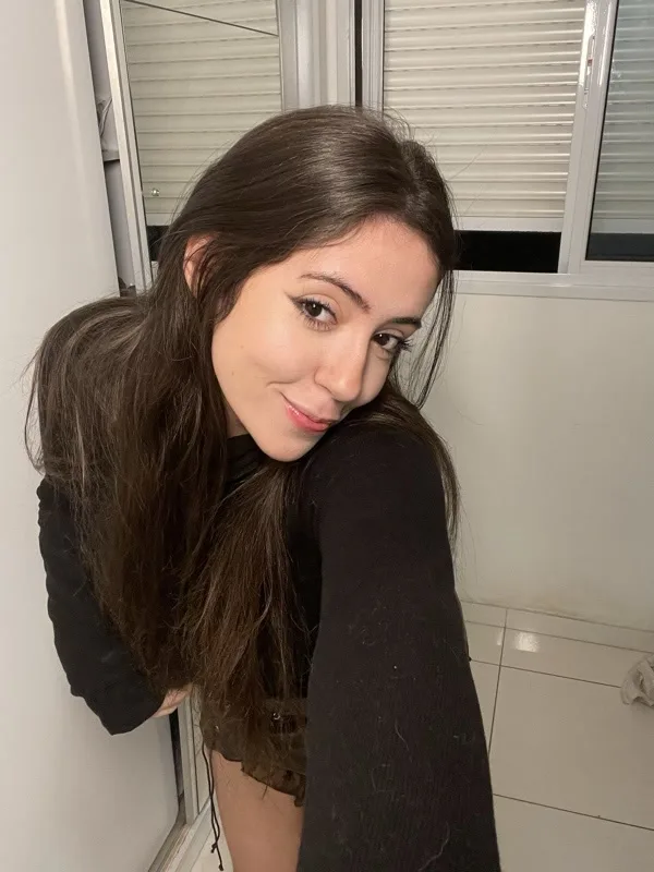 Brunna Funchal apoiada na parede do corredor de casa, sorrindo